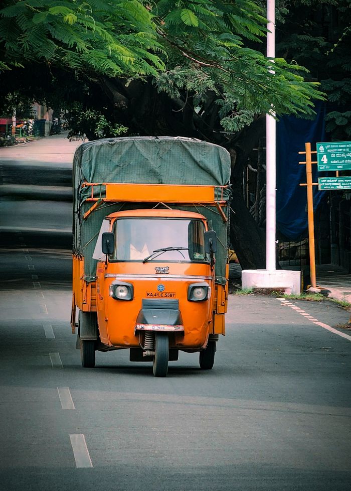 Vibrant orange auto rickshaw on a quiet road in Bengaluru, India, surrounded by greenery.