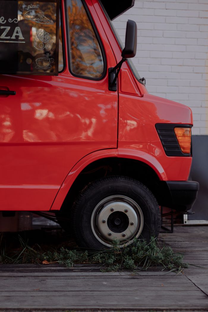About Close-up of a red food truck parked outdoors amidst greenery, highlighting vehicle details.