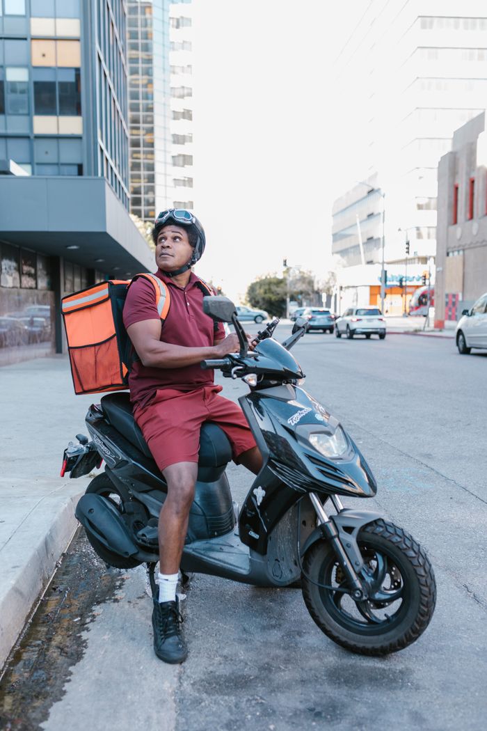 Mastering the First Impression: Your intriguing post title goes here A delivery rider in uniform on a motorcycle, ready for urban delivery.